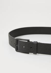 Schwarzer Lederumgurt mit strukturiertem Finish, ausgestattet mit einerMetallschnalle und mehreren Einstelllöchern. Schlichtes, flaches Design.