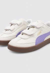 Zapatillas sintéticas blancas con acentos morados, correas de velcro y suela de goma marrón. Presentan un material texturizado y un diseño cosido.