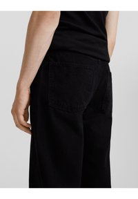 Pantalones de mezclilla negros con un corte holgado, que cuentan con dos bolsillos traseros y un acabado sutilmente texturizado, mostrados desde los lados y desde atrás.