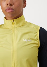 Gelbe Radfahrweste mit hohem Kragen, leichtem Stoff, Reißverschluss vorne und dem weißen "Rapha"-Logo auf der linken Brust.