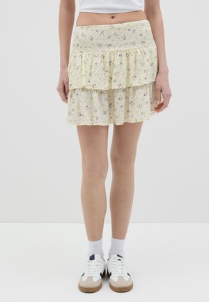 Jupe tiered jaune à fleurs avec une taille smockée, ornée de petites fleurs multicolores et d'une texture légère et transparente. Portée avec des baskets blanches.