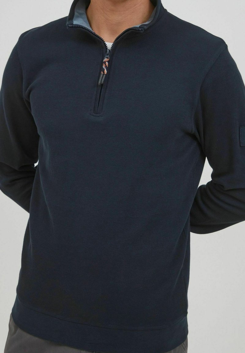 Navyblauer Zip-Kragen-Pullover aus geripptem Stoff. Verfügt über einen kontrastierenden inneren Kragen und ein Patch am linken Ärmel.