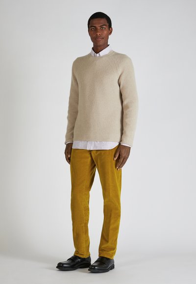 Beige geribbelde brei trui, met daaronder een wit-blauw gestreepte blouse, gele corduroybroek en zwarte schoenen. Eenvoudig modern ontwerp.