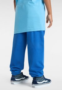 Blauwe trainingsbroek met elastische boorden, gemaakt van zacht materiaal. Draagt bij navy sneakers met witte accenten en gestreepte sokken.