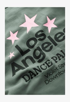 Zaļš audums ar lieliem melniem burtiem, kuros ir rakstīts "Los Angeles" un "DANCE PALACE". Virs teksta ir divas rozā zvaigznes ar izšūtiem elementiem.