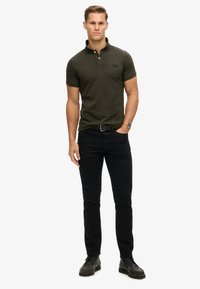 Mørkeblå polo skjorte med en tre-knaps stolpe, korte ærmer og broderet logo. Parret med tætsiddende sorte jeans og sorte sko.