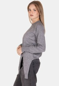 Maglione grigio a maniche lunghe in maglia con colletto a girocollo e spacchi laterali. Abbinato a jeans scuri, che mostrano una vestibilità rilassata e una texture liscia.