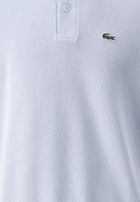 Pikétröja i ljusblått med en ribbad textur, två-knapps knäppning och en liten grön krokodil-logotyp på vänster bröst.