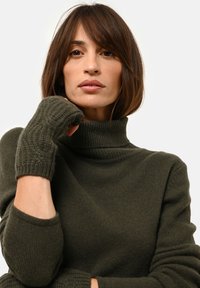 Oliwkowy sweter z golfem wykonany na drutach z ribbowanymi mankietami i bezpalczastymi rękawicami. Miękka faktura, luźny krój i wyraźny kołnierz.