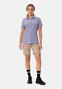 Korte mouwen geruit overhemd in paars, beige shorts, zwarte sokken met witte strepen en zwarte schoenen met oranje accenten. Casual outdoor outfit.