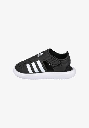 Sandalia negra tipo slip-on de Adidas con rayas blancas, aberturas laterales de ventilación y suela blanca acolchada.