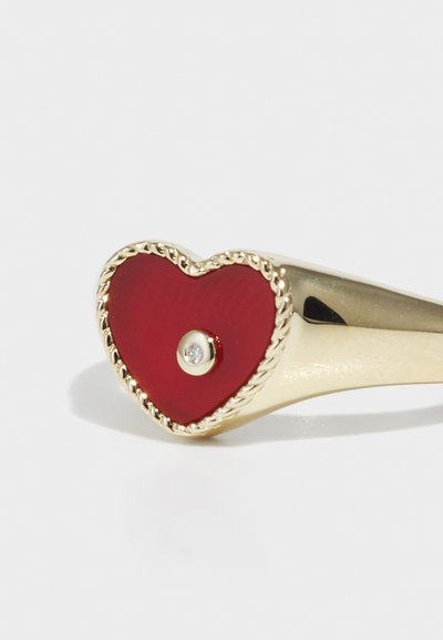 Inel de aur cu un design în formă de inimă roșie, având o suprafață texturată, o mică piatră prețioasă transparentă în centru și accente de aur torsionat în jurul marginii.