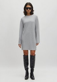 Graues, geripptes Kleid mit langen Ärmeln, Rundhalsausschnitt und lockerer Passform, kombiniert mit knielangen schwarzen Lederstiefeln und großen schwarzen Sonnenbrillen.