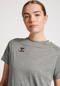 Grå kortærmet atletisk t-shirt lavet af letvægtsstof, med et sort logo på brystet og en rund halsudskæring.