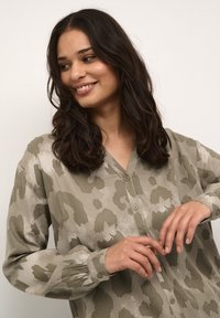 Blusa de manga larga, con botones, en un tejido verde apagado con un estampado de leopardo. Presenta un escote en forma de V y puños abotonados.