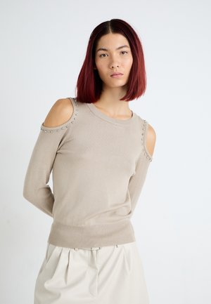 Maglione beige a maglia con design a spalla fredda, impreziosito da borchie metalliche lungo le cuciture delle spalle e un orlo a costine aderente.