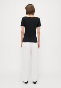 Top preto de manga curta com um decote largo, combinado com calças brancas largas com bolsos traseiros e um tecido leve.