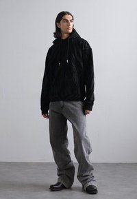 Hanorac texturat negru cu glugă, asortat cu blugi gri largi și pantofi slip-on negri. Design minimalist, paletă de culori simplă.