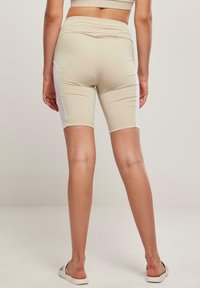Bézs színű kerékpáros rövidnadrág magas derékpánttal, fehér oldalsó panelekkel és sima, rugalmas anyaggal. Minimalista dizájn, látható logók nélkül.