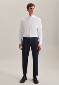 Chemise blanche à manches longues avec un col boutonné, associée à un pantalon bleu marine ajusté et des chaussures en cuir noir. Design simple, sans motifs.