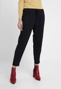 Schwarze tapered Hosen mit Falten, elastischem Bund und Seitentaschen, kombiniert mit roten Lederstiefeletten mit spitzem Zehen.