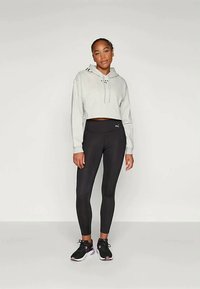 Pilkos spalvos trumpas džemperis su raišteliu, juodos spalvos leginsai ir juodi sportiniai bateliai su rožinėmis detalėmis. Lygus audinys, prigludęs dizainas.