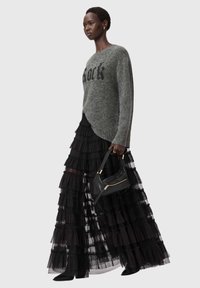 Harmaa neulepaita, jossa on paljetilla koristeltu teksti, kerroksellinen musta tyllimallinen maxihame ja pieni musta käsilaukku, jossa on kultaiset yksityiskohdat.