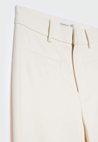 Pantalon beige avec une taille plate, passants pour ceinture et deux poches avant. Confectionné dans un tissu lisse avec une coupe ajustée.