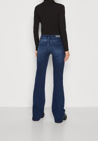 Dunkelblaue Schlagjeans mit einem ausgewaschenen Finish, aus Denim gefertigt. Besitzt zwei Gesäßtaschen und ein Lederetikett am Bund.