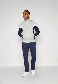 Gray zip-up jacket with white and navy sleeves, paired with navy sweatpants; cotton blend, with logo accents and ribbed cuffs.