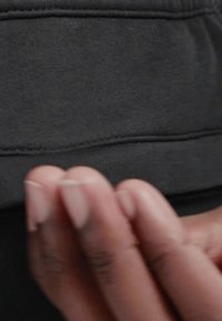 Černá tkanina s viditelnou texturou a ševy, na které je ruka držící okraj. Jednoduchý design, bez dalších vzorů nebo kovových součástí.