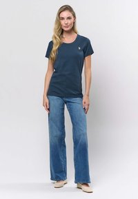 Mornarsko plava pamučna majica s okruglim izrezom, kratkim rukavima i sitnim detaljem logotipa na prsima, uparena sa svijetloplavim trapericama širokih nogavica.