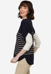 Námorníkový pruhovaný top s béžovými horizontálními pruhy, krátkými rukávy a volným střihem. Materiál vypadá měkký s jemnou texturou.