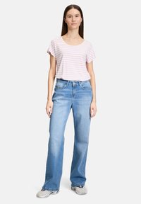 Haut à manches courtes rayé rose et blanc associé à un jean large bleu clair. Tissu texturé avec une coupe décontractée. Porté avec des baskets grises.