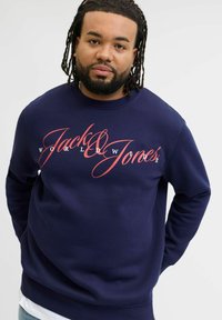 Sudadera azul marino con un atrevido diseño gráfico en rojo que dice "Jack & Jones World Wide." Fabricada con un tejido suave y texturizado.