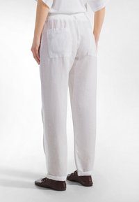 Valkoiset pellavahousut rentoutuneella istuvuudella, joissa on kaksi takataskua ja käärittyjä lahkeensuita, korostaen teksturoitua kangasta.