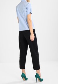 Chemise légère bleu clair à manches courtes associée à un pantalon noir coupé et des chaussures à talons hauts teal. Tissu lisse et coupe ajustée.
