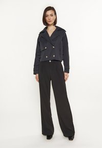 Giacca cropped nera doppiopetto con grandi bottoni metallici, abbinata a pantaloni neri a gamba larga a vita alta. Tessuto liscio, design strutturato.