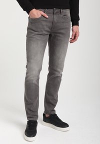 Harmaat farkut slim fit -mallilla, joissa on hieno haalistuminen ja viisi taskua. Mallilla on mustat lenkkarit, jotka täydentävät rentoa ilmettä.