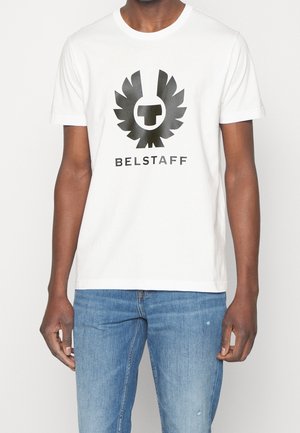 Weißes Baumwoll-T-Shirt mit großem schwarzen Adler-Logo und zentralem Emblem, sowie dem Text "BELSTAFF" darunter in fetter schwarzer Schrift. Lockerer Schnitt.