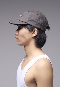 Sapca prezintă un material textil gri închis cu modele de stropi roșii, o cozoroc curbat și o etichetă cu logo lateral. Curea ajustabilă în partea din spate.