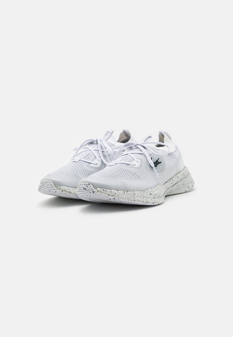 Baskets de sport blanches avec une tige en tricot texturé, fermeture à lacets et une semelle intermédiaire mouchetée. Présente un petit logo sur le côté.