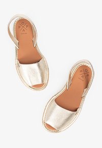 Sandalias metálicas doradas con una parte superior texturizada, punta abierta y una correa trasera. La plantilla marrón presenta un logotipo en relieve. Bordes envueltos en yute.