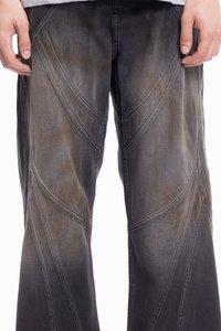 Črne jeans hlače ohlapnega kroja, ki imajo diagonalne šive in postopno zbledenje, kar poudarja teksturo in oblikovne podrobnosti.