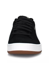 Zapatillas de ante negro con detalles blancos y suela de goma marrón. Presentan cordones planos y un diseño de punta redondeada. Textura suave en general.