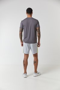 Grå t-skjorte med korte ermer i atletisk stil kombinert med lysegrå shorts med gule sideakenter, viser tatoveringer og hvite joggesko.