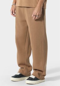 Ruske trenirke med relaxed fit, z bočnimi šivi in mehkimi teksturami. V kombinaciji s črnimi športnimi copati z belimi vezalkami in krema barvo podplata.