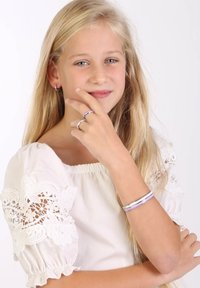 Zilveren en paarse ringen en een armband om de hand van een meisje. Ze draagt een witte jurk met kantmouwen. Lang, steil blond haar.