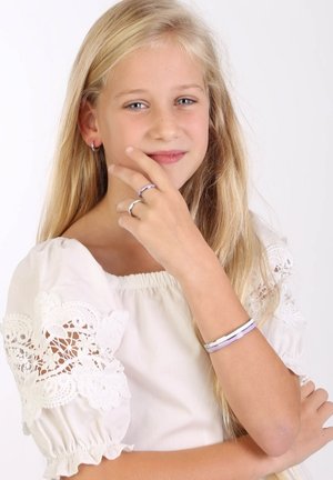 Zilveren en paarse ringen en een armband om de hand van een meisje. Ze draagt een witte jurk met kantmouwen. Lang, steil blond haar.