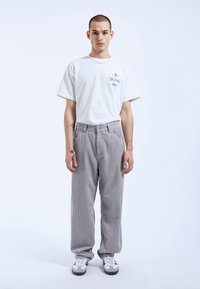 Grijze ribcord broek met een relaxed fit, gecombineerd met een plain wit t-shirt en witte sneakers met zwarte accenten.
